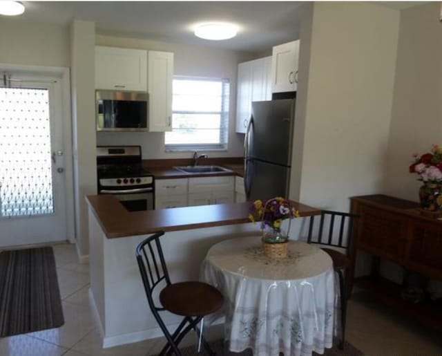 kitchen with white cabinetry, sink, light tile patterned floors, kitchen peninsula, and stainless steel appliances