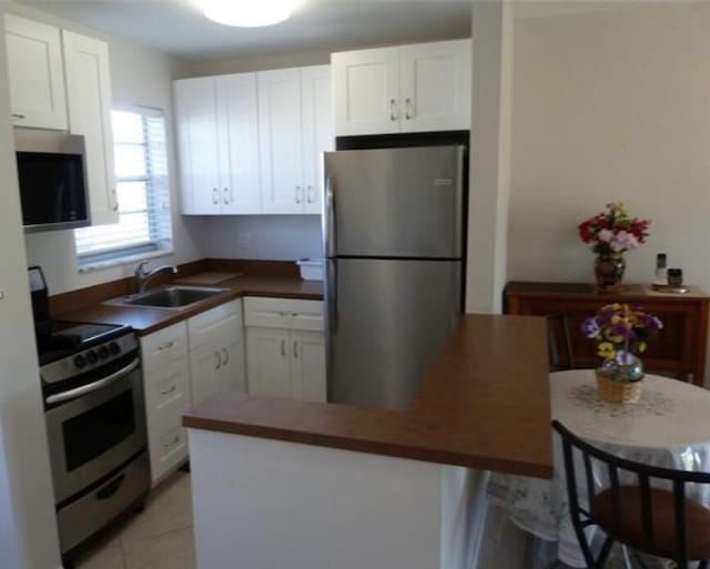 kitchen featuring sink, white cabinetry, stainless steel appliances, a kitchen breakfast bar, and light tile patterned flooring