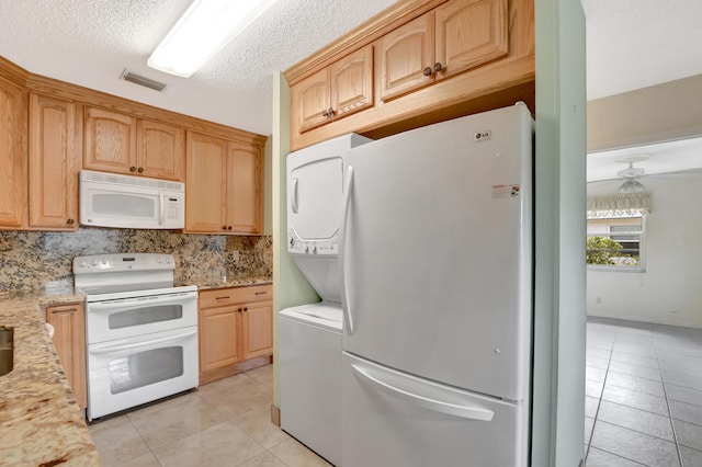 kitchen featuring light stone counters, white appliances, stacked washer and clothes dryer, and decorative backsplash