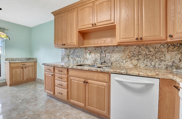 kitchen featuring light stone counters, white dishwasher, sink, and decorative backsplash