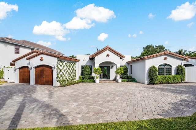 mediterranean / spanish house with a tile roof, an attached garage, a gate, decorative driveway, and stucco siding