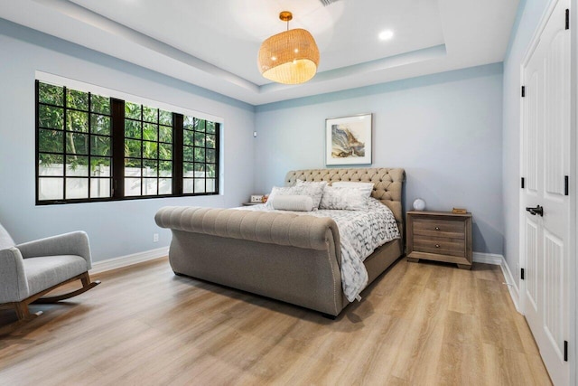 bedroom with light wood-type flooring, a raised ceiling, and baseboards