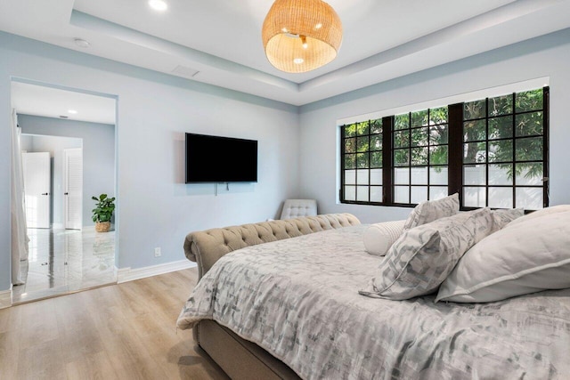 bedroom featuring baseboards, a tray ceiling, wood finished floors, and recessed lighting