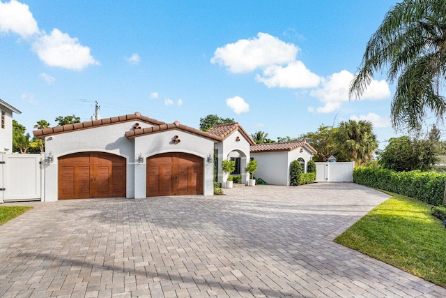 mediterranean / spanish home with decorative driveway, a tile roof, stucco siding, an attached garage, and a gate