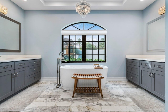 full bath with marble finish floor, a freestanding bath, vanity, and baseboards