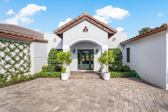 view of exterior entry with french doors, a tile roof, and stucco siding