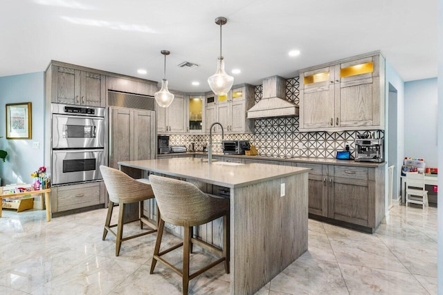 kitchen featuring a center island with sink, custom exhaust hood, visible vents, double oven, and a sink