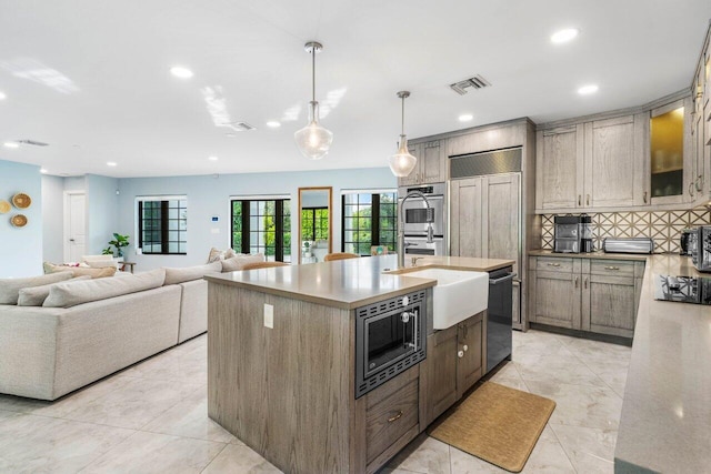 kitchen featuring built in appliances, a sink, visible vents, backsplash, and an island with sink