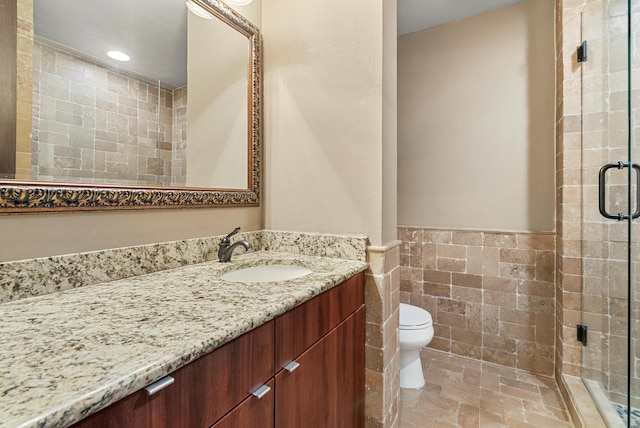 full bathroom with toilet, a wainscoted wall, vanity, a shower stall, and tile walls