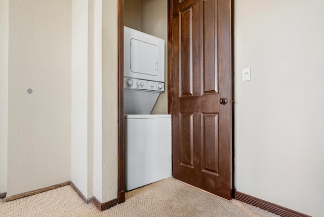 clothes washing area featuring baseboards, stacked washer and dryer, and light colored carpet