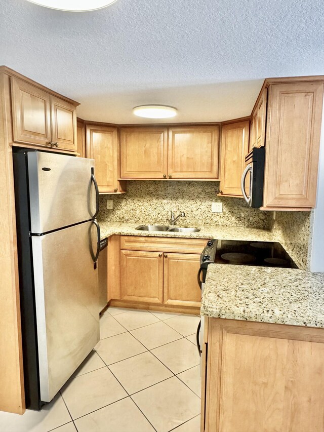 kitchen featuring light tile patterned flooring, light stone counters, a sink, a textured ceiling, and stainless steel appliances
