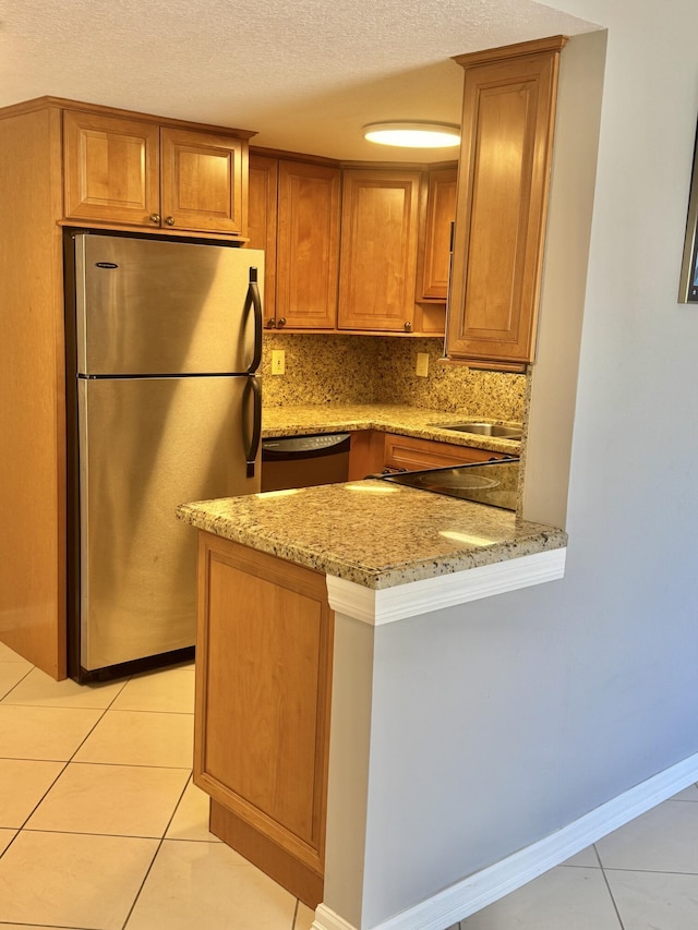 kitchen featuring brown cabinetry, a textured ceiling, appliances with stainless steel finishes, light tile patterned floors, and a peninsula