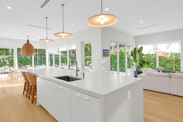 kitchen with sink, white cabinetry, decorative light fixtures, a kitchen island with sink, and light hardwood / wood-style floors