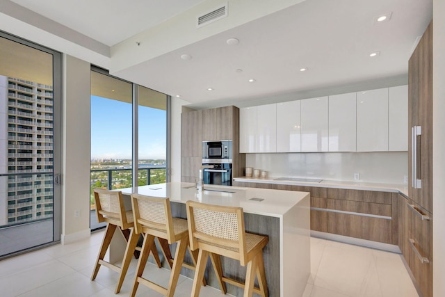 kitchen with light tile patterned flooring, oven, white cabinets, a kitchen bar, and a kitchen island with sink