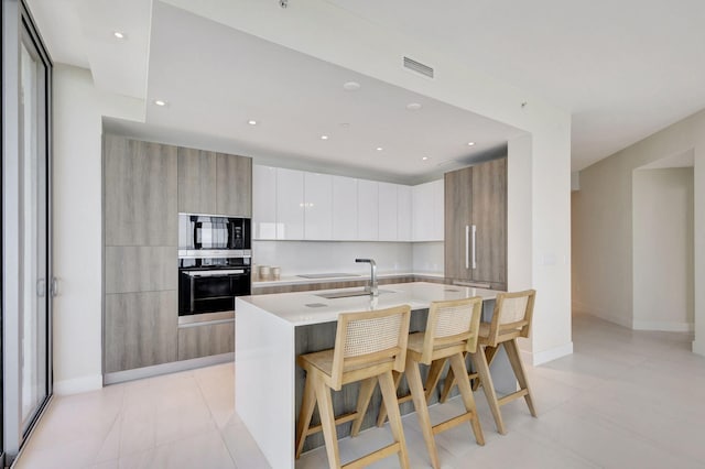 kitchen featuring sink, a breakfast bar area, black microwave, an island with sink, and oven