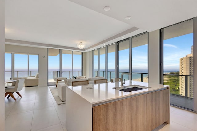 kitchen featuring floor to ceiling windows, sink, a water view, light tile patterned floors, and an island with sink