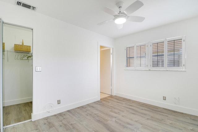 unfurnished bedroom featuring a spacious closet, a closet, ceiling fan, and light wood-type flooring