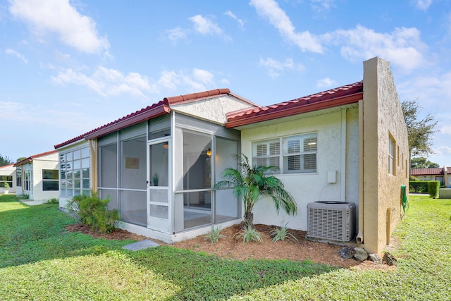 back of property featuring a sunroom, central AC, and a lawn