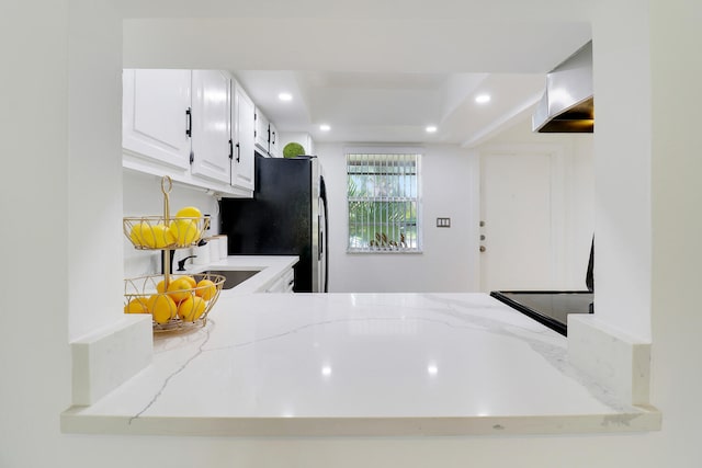 kitchen with stainless steel fridge, sink, white cabinets, and light stone counters