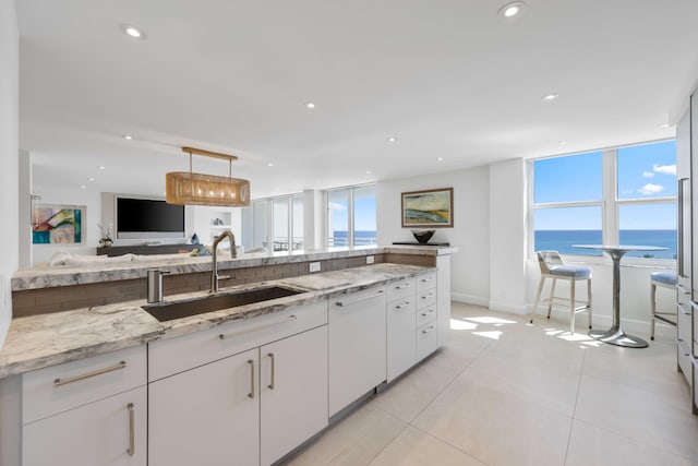 kitchen featuring pendant lighting, sink, white cabinetry, a water view, and light stone countertops