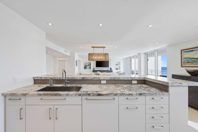 kitchen with white cabinetry, light stone countertops, sink, and kitchen peninsula