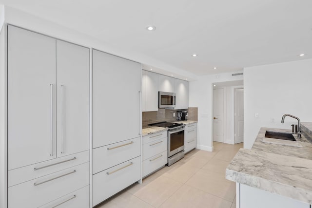 kitchen featuring appliances with stainless steel finishes, white cabinetry, sink, decorative backsplash, and light tile patterned floors