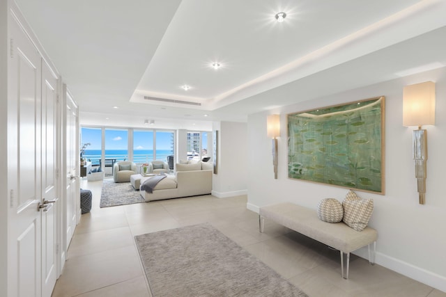 living room featuring a raised ceiling, a water view, and light tile patterned floors