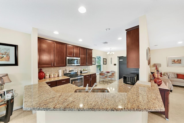 kitchen featuring sink, appliances with stainless steel finishes, tasteful backsplash, light stone countertops, and kitchen peninsula