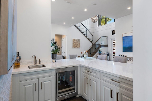 interior space with wine cooler, light stone countertops, sink, and kitchen peninsula