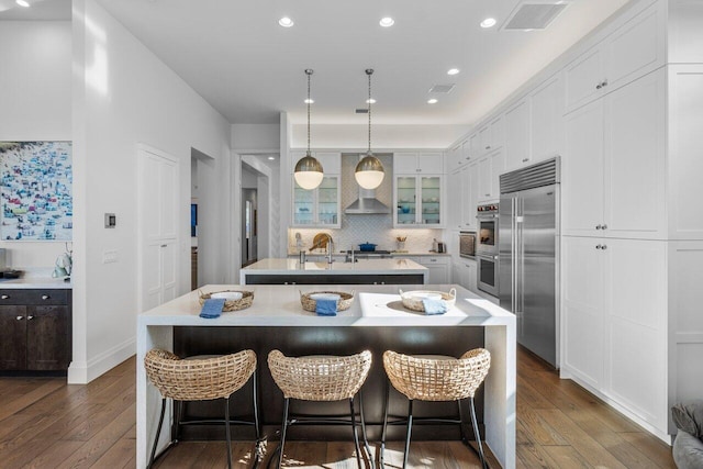 kitchen featuring stainless steel appliances, white cabinetry, pendant lighting, and a center island with sink