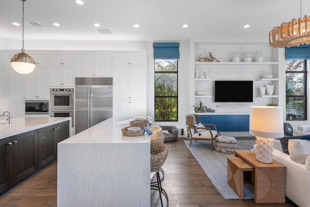 kitchen featuring white cabinetry, built in appliances, light stone countertops, and pendant lighting