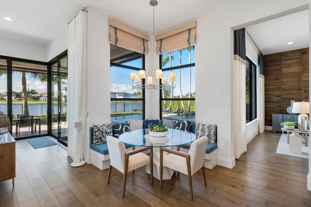 dining space with a water view, a notable chandelier, wood walls, and hardwood / wood-style flooring