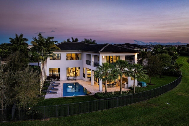 back house at dusk featuring a balcony, a yard, a fenced in pool, and a patio