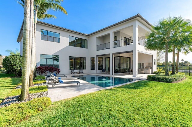 back of property with a fenced in pool, a lawn, a patio, a balcony, and exterior kitchen