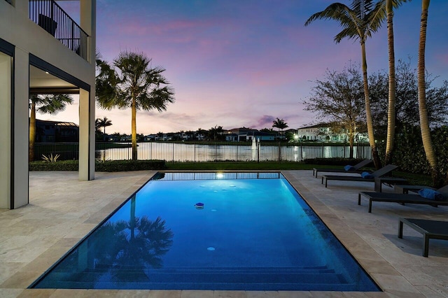 pool at dusk featuring a water view and a patio area