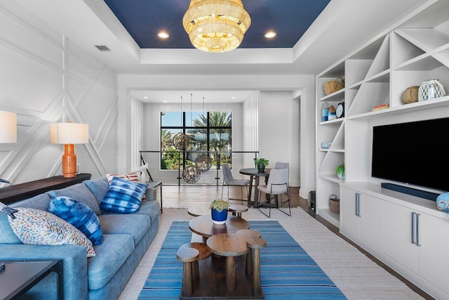 living room featuring a raised ceiling, built in features, a chandelier, and light hardwood / wood-style floors