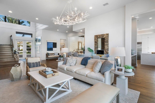 living room featuring french doors, a towering ceiling, an inviting chandelier, and hardwood / wood-style flooring