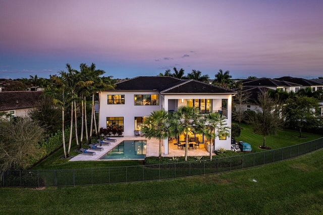 back house at dusk with a fenced in pool, a patio, and a lawn