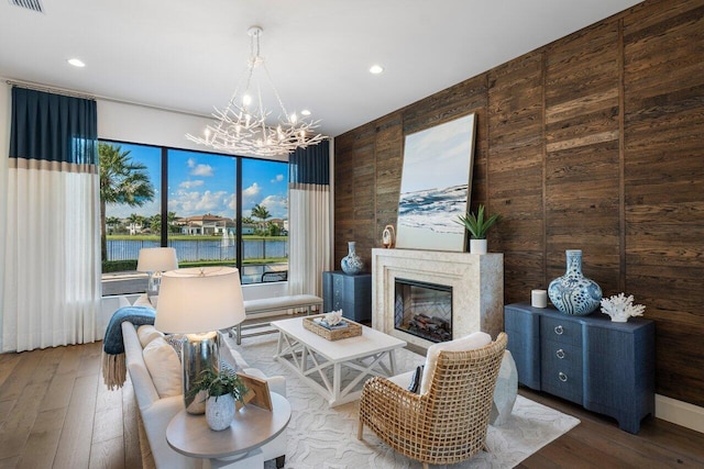 living room featuring a fireplace, wood walls, wood-type flooring, a chandelier, and a water view