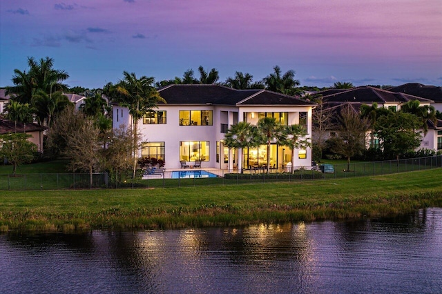 back house at dusk with a fenced in pool, a balcony, a water view, and a yard