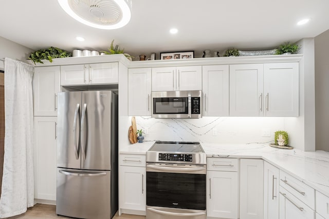 kitchen featuring stainless steel appliances, light stone countertops, light hardwood / wood-style floors, tasteful backsplash, and white cabinets