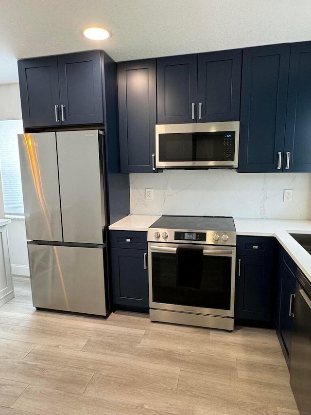 kitchen featuring light countertops, appliances with stainless steel finishes, decorative backsplash, and light wood-style floors