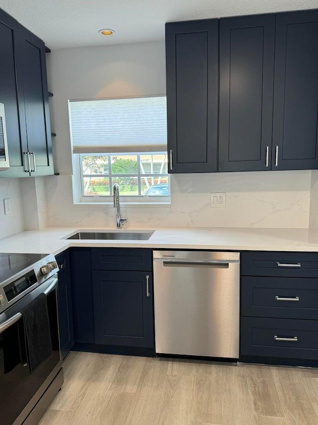 kitchen with appliances with stainless steel finishes, light wood-type flooring, light countertops, and a sink