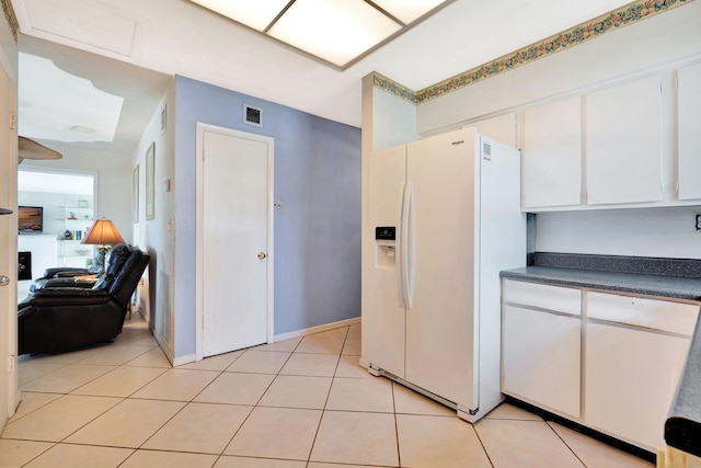 kitchen featuring white cabinetry, white refrigerator with ice dispenser, and light tile patterned flooring