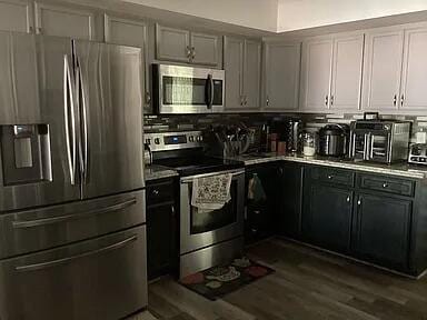 kitchen with gray cabinetry, dark wood-type flooring, tasteful backsplash, and appliances with stainless steel finishes