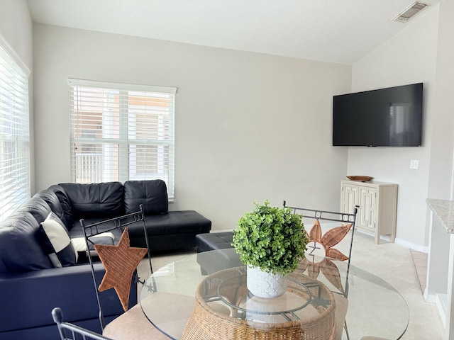 living area featuring lofted ceiling, visible vents, light carpet, and baseboards
