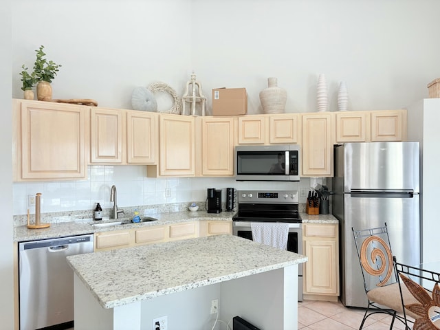 kitchen featuring a sink, appliances with stainless steel finishes, a kitchen island, and light stone countertops