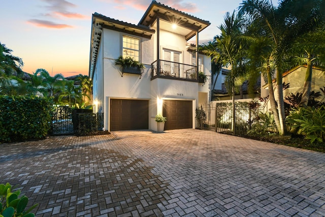 mediterranean / spanish house featuring a garage, a balcony, fence, decorative driveway, and stucco siding