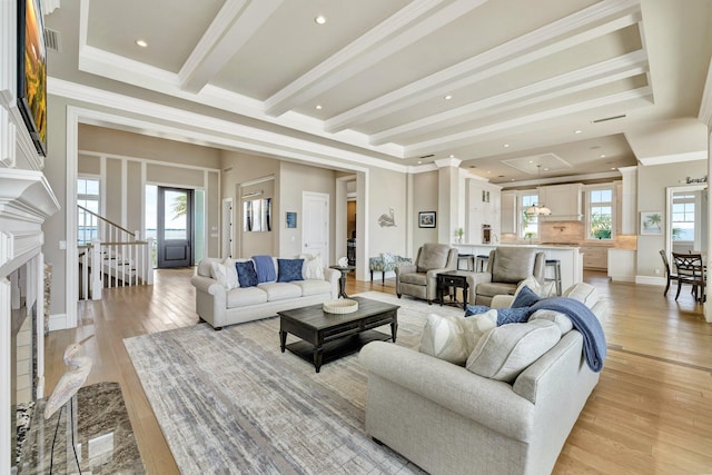 living area with light wood-style floors, ornamental molding, beamed ceiling, and a premium fireplace