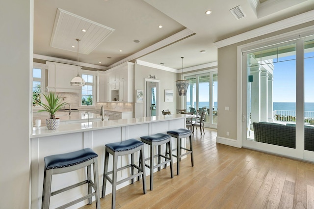 kitchen featuring light wood finished floors, light countertops, visible vents, backsplash, and ornamental molding